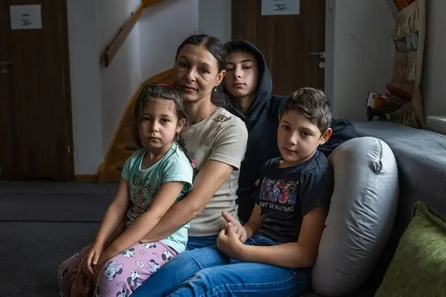 A woman sits on a sofa embracing a young girl, while two older children sit next to them
